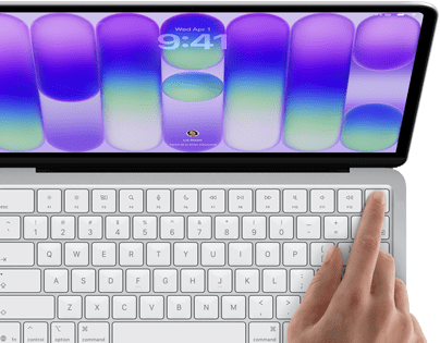 MacBook Neo, stříbrná barva, zobrazuje se přihlašovací obrazovka, něčí prst na snímači Touch ID v pravém horním rohu klávesnice