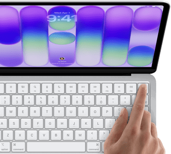 MacBook Neo, stříbrná barva, zobrazuje se přihlašovací obrazovka, něčí prst na snímači Touch ID v pravém horním rohu klávesnice