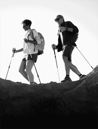 Zwei Personen mit einer Apple Watch am Handgelenk, Trekkingstöcken und anderer Ausrüstung auf einem felsigen Pfad